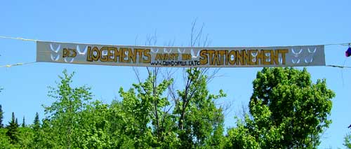« Des logements avant un stationnement » : la bannière tendue entre les arbres à l'entrée du site, avec l'adresse du site web, juin 2003.